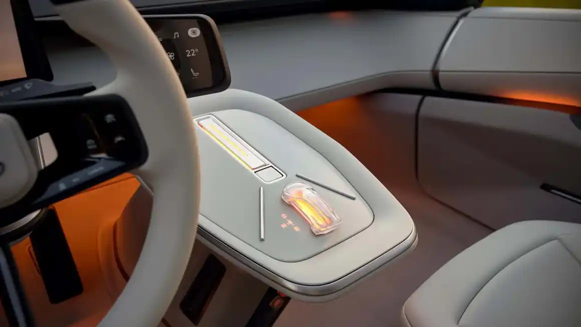 A close-up view of a futuristic car interior featuring a minimalist design with smooth, touch-sensitive panels, an innovative gear selector, and ambient lighting.