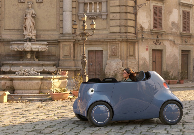 Woman driving small modern blue Fiat Topolino XS on scenic cobblestone square