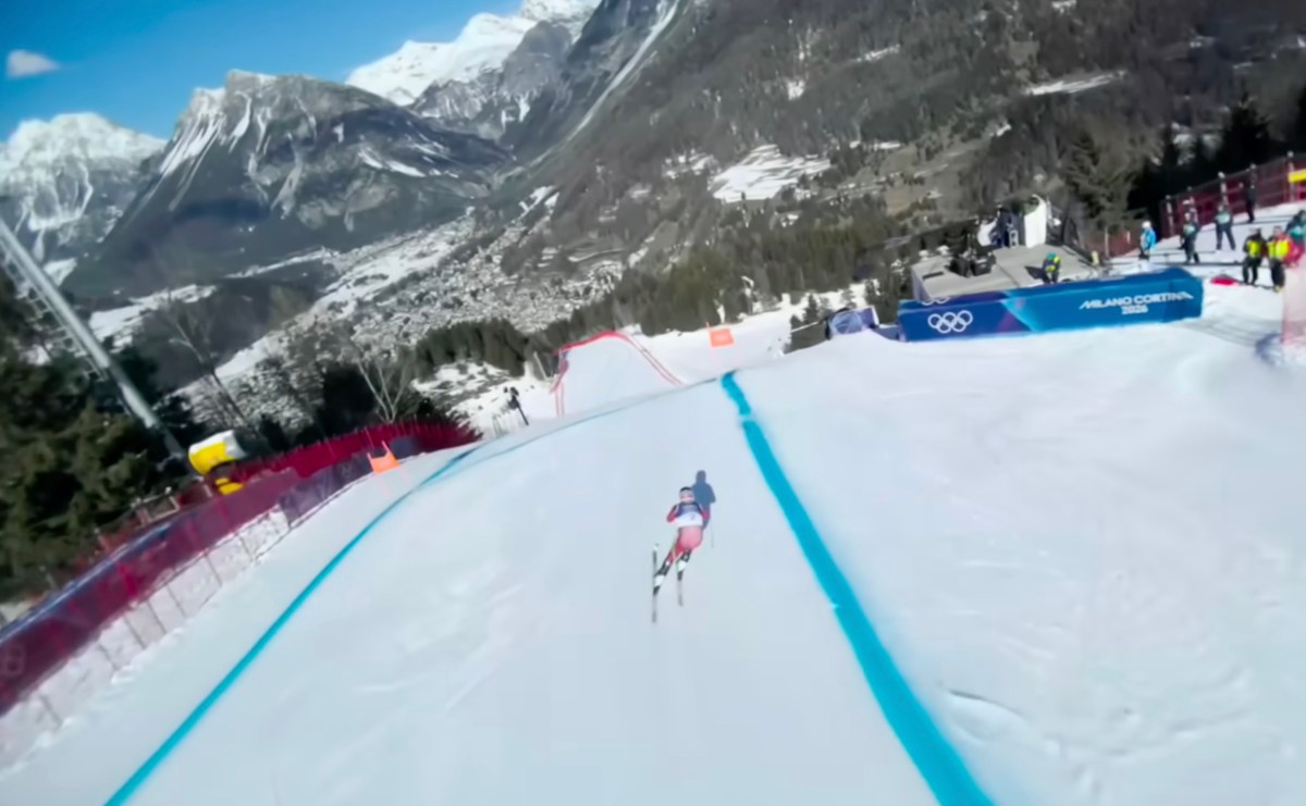 Skier racing down snowy slope with blue lines surrounded by spectators Milan Cortina