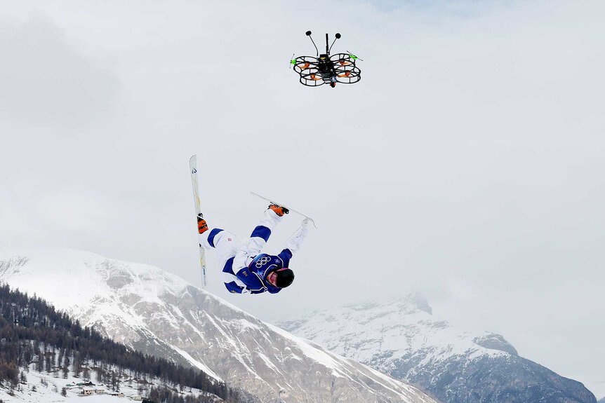 Skier performing mid-air flip above snow-covered mountain range Milan Cortina 2026 Olympics